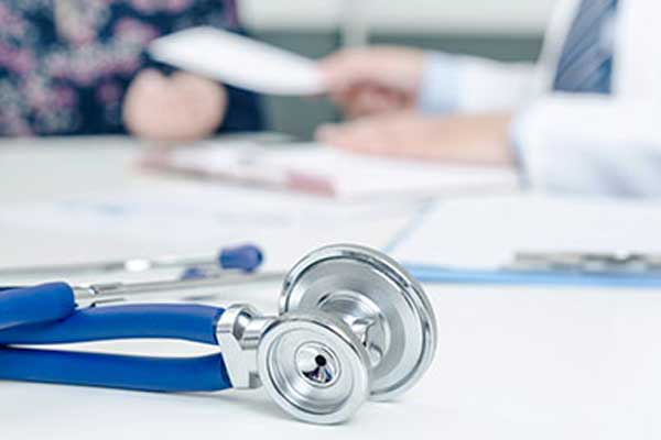 Stethoscope on a desk in the background you can see a doctor handing paper to a woman